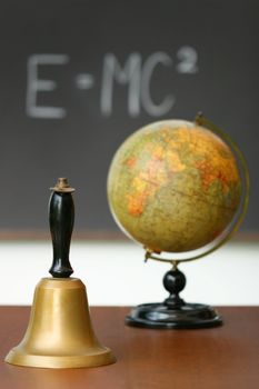 Old school bell on desk in front of chalkboard
