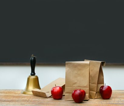Paper lunch bags with apples and school bell on desk