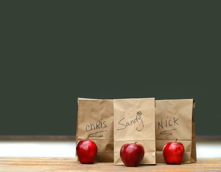 Lunch bags on desk with red apples in front of green chalkboard