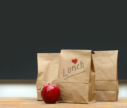 Paper lunch bags with red apple on school desk