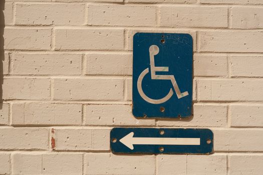 A handicapped sign and arrow on a brick white wall.