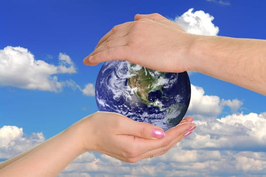 male and female hands holding the earth on background the sky
