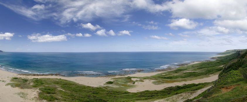 It is a beautiful panoramic coastline with blue sky and green grassland.