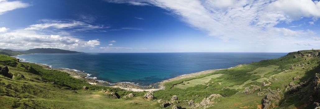 It is a beautiful panoramic coastline with blue sky and green grassland.