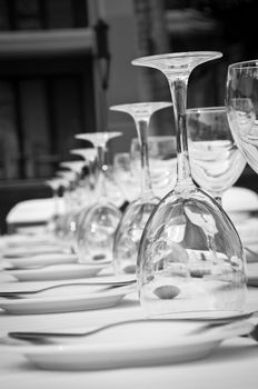 Black & white close-up of a wedding receptions' dinner table with plates, water & wine glasses lined up into the distance.