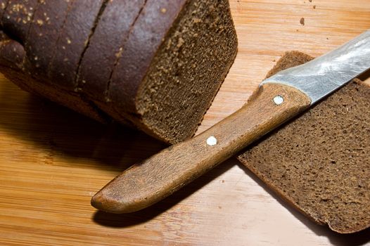 Loaf of black bread and knife on wooden board