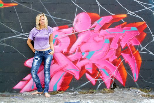 A lovely young blonde leans against a graffiti-covered wall.