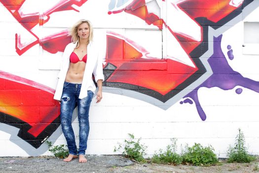 A lovely young blonde leans against a graffiti-covered wall.