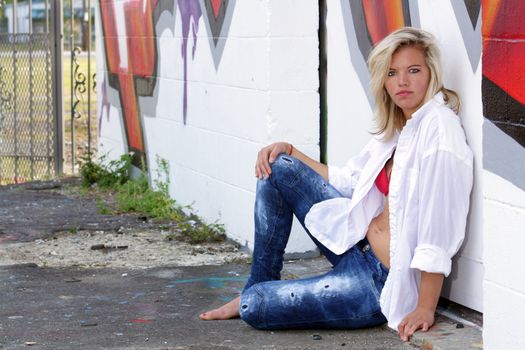 A lovely young blonde leans against a graffiti-covered wall.