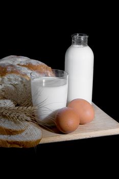 Bottle and cup of milk, eggs and bread on black