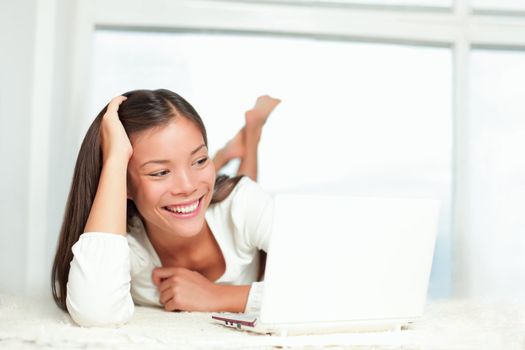 Laptop woman at home smiling at PC screen laughing. Casual Asian / Caucasian young woman lying on the floor looking at the computer