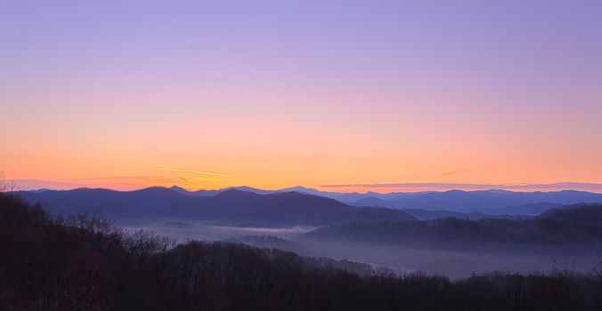 Sun rising over snowy mountains of Smokies in early spring with fog in valleys