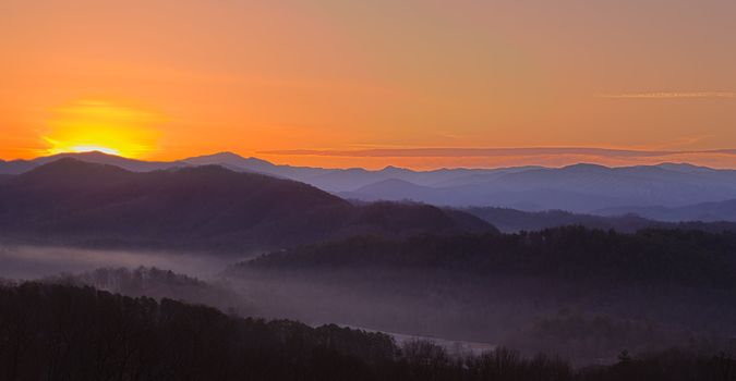 Sun rising over snowy mountains of Smokies in early spring with fog in valleys