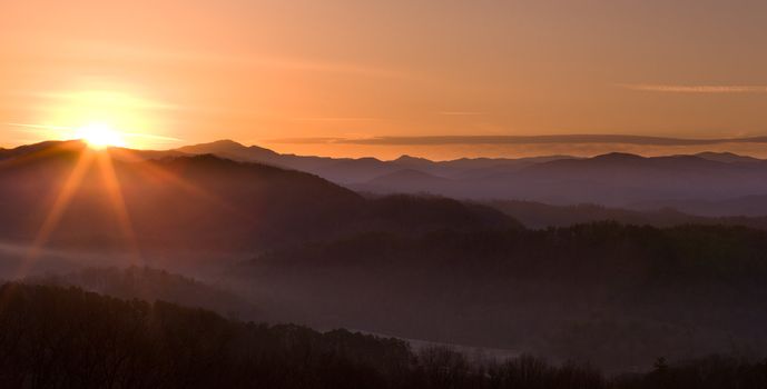 Sun rising over snowy mountains of Smokies in early spring with fog in valleys