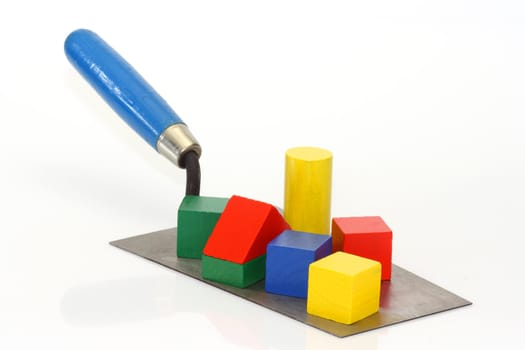 Trowel with toy bricks on bright background