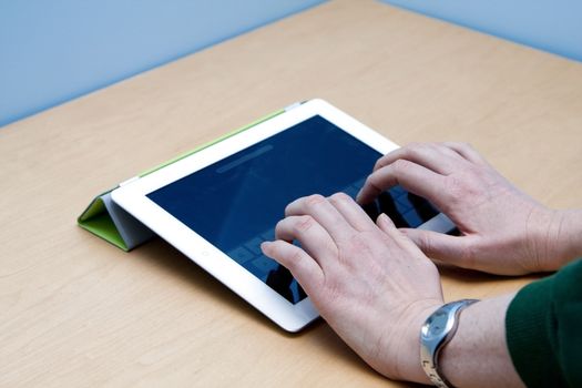 Female user hands typing on the new iPad 2 from Mac Apple, on a wooden desk and blue background.