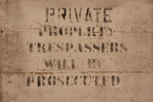 faded private property, trespassers will be prosecuted sign painted on a concrete wall 