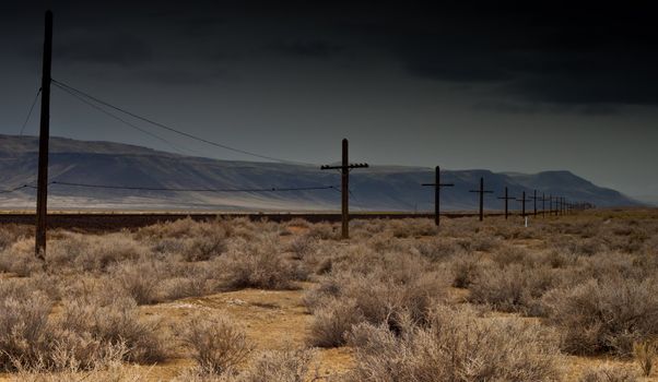 A photograph of an old desert railroad.  The storm is coming in and the mountains are pushing the clouds up.