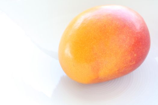 Fresh whole mango on a white plate