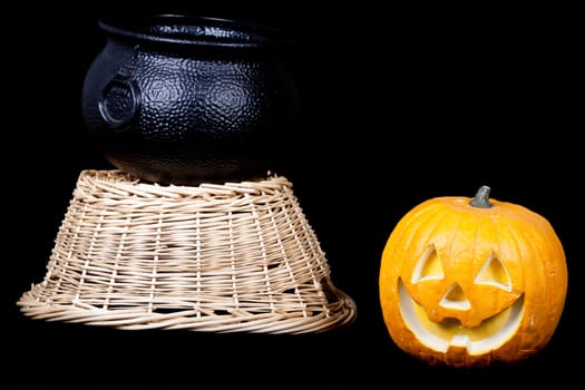 A pumpkin, harvest basket and a cauldron on black.