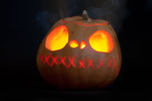 Halloween carved pumpkin, glowing and smoking in the dark