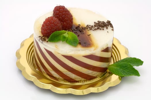 Caramel mousse cake on a golden plate decorated with raspberries and mint leaves