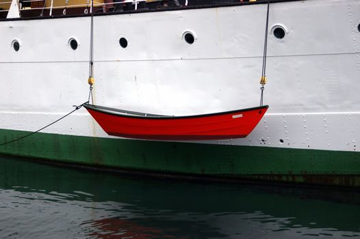 A dory, dingy, lifeboat or small row boat being lowered to the water over the side of a ship.