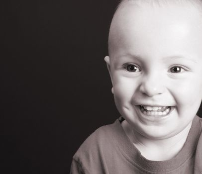 Blonde toddler against a black background with a big smile