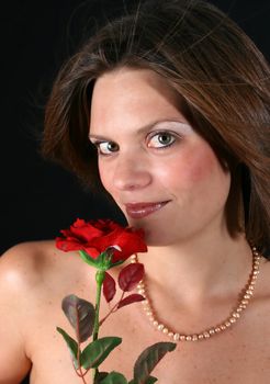 Beautiful young woman with a red rose and pearls