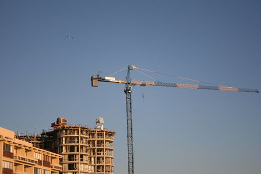 High Crane against a blue sky close to a building site
Building Crane behind other buildings with construction to the right