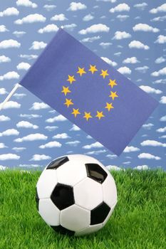 Soccerball on grass with european flag over sky background