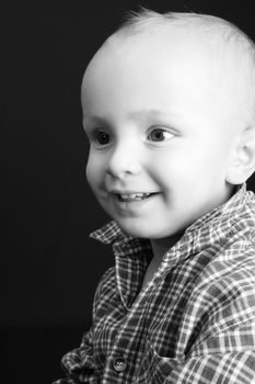 Blonde toddler against a black background with a big smile