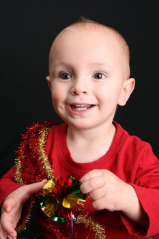 Toddler against a black background playing with christmas decorations