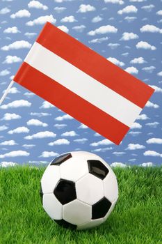 Soccerball on grass with austrian national flag over sky background