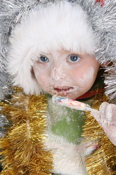 Toddler covered with christmas decorations after baking, eating a lollie