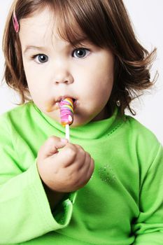 Toddler girl with chubby cheeks eating a sticky lollipop