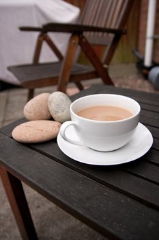 Outdoor cup of tea in a white cup and saucer with stones on a wooden background