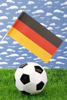 Soccerball on grass with german national flag over sky background