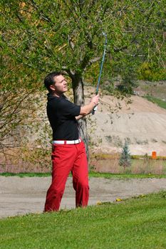Young male golfer playing a shot from the bunker