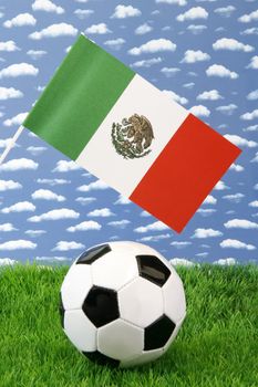 Soccerball on grass with mexican national flag over sky background