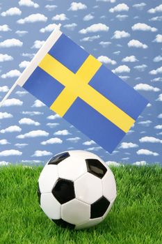 Soccerball on grass with swedisch national flag over sky background
