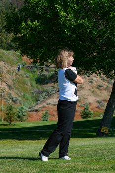 Blond female golfer following her ball down the fairway