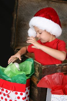 Cute boy sitting inside an antique trunk playing with a decorative christmas ball