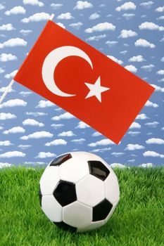 Soccerball on grass with turkish national flag over sky background
