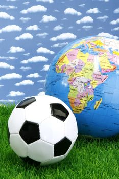 Soccerball on grass with globe over sky background