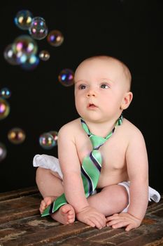 Cute baby boy sitting on an antique trunk looking at bubbles