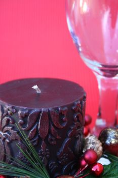 Dark candle with a christmas wreath and a wine glass on a red background