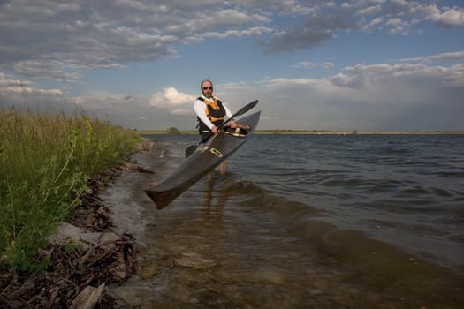 mature paddler launching long racing carbon fiber kayak on a lake with grassy and rocky shore in northern Colorado, thirteen - temporary race number placed on deck by myself