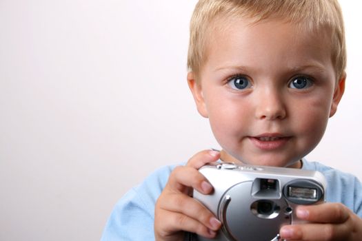 Shy toddler holding a silver camera, looking at his object
