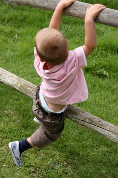 Young boy climbing on wooden fencing on a farm
